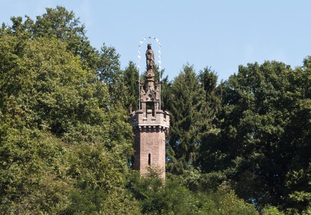 Die Mariensäule in Kyllburg ragt aus dichtem Wald hervor. Eine Statue steht auf einem steinernen Turm, umgeben von grünen Bäumen und blauem Himmel., © TI Bitburger Land Die Mariensäule in Kyllburg ragt aus dichtem Wald hervor. Eine Statue steht auf einem steinernen Turm, umgeben von grünen Bäumen und blauem Himmel., © TI Bitburger Land