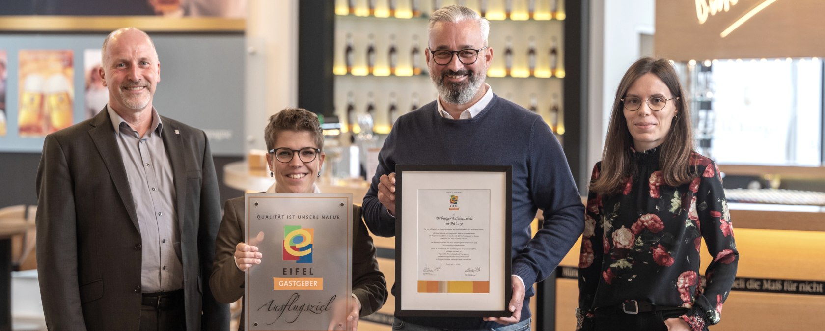 Marco Boor, Leiter Regionales Marketing und Sponsoring Bitburger, und Susanna Schneider, Gästebegleiterin und Q-Coach der Bitburger Erlebniswelt, nehmen die EIFEL Gastgeber-Plakette von Markus Pfeifer und Alina Wonner in Empfang, © Bitburger / Harald Tittel Marco Boor, Leiter Regionales Marketing und Sponsoring Bitburger, und Susanna Schneider, Gästebegleiterin und Q-Coach der Bitburger Erlebniswelt, nehmen die EIFEL Gastgeber-Plakette von Markus Pfeifer und Alina Wonner in Empfang, © Bitburger / Harald Tittel