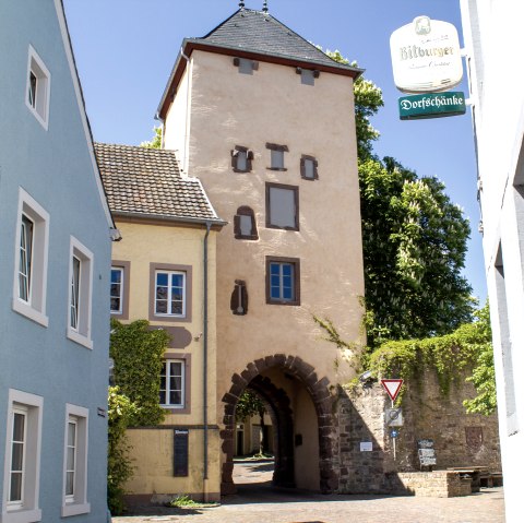 Das Oberes Tor in Dudeldorf, ein historisches Stadttor, umgeben von bunten Häusern und einem Straßenschild. Sonniger Tag mit blauem Himmel., © Tourist-Information Bitburger Land_M. Mayer Das Oberes Tor in Dudeldorf, ein historisches Stadttor, umgeben von bunten Häusern und einem Straßenschild. Sonniger Tag mit blauem Himmel., © Tourist-Information Bitburger Land_M. Mayer