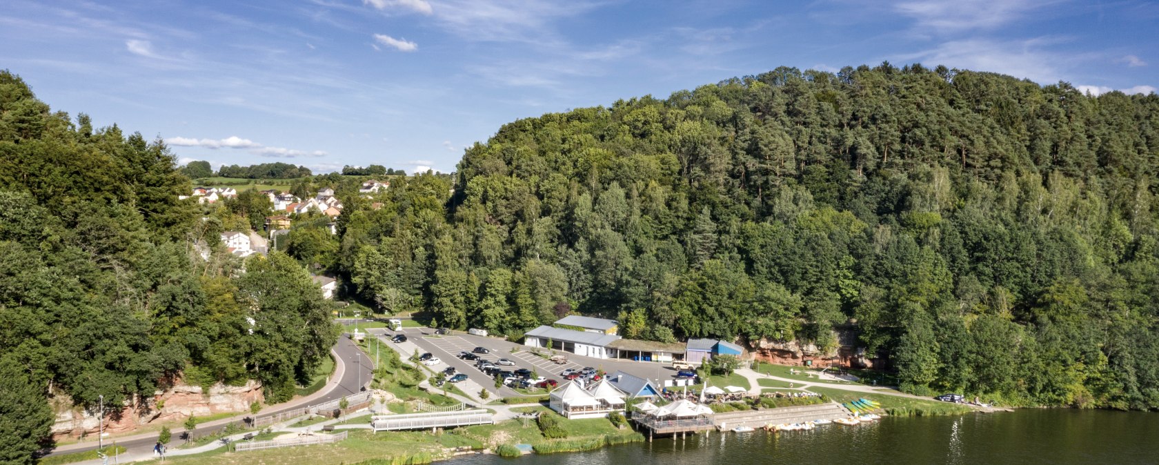 Vue aérienne du lac de barrage de Bitburg avec la forêt adjacente, les bâtiments et les parkings. Le ciel est clair et bleu., © team360 B. Treib Vue aérienne du lac de barrage de Bitburg avec la forêt adjacente, les bâtiments et les parkings. Le ciel est clair et bleu., © team360 B. Treib