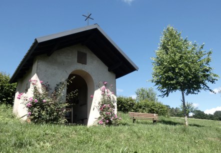 Petite chapelle dans la verdure, entourée de roses en fleurs. Un banc se trouve à côté, un arbre fait de l'ombre. Ciel bleu en arrière-plan., © Tourist-Information Bitburger Land, Melanie Salzburger Petite chapelle dans la verdure, entourée de roses en fleurs. Un banc se trouve à côté, un arbre fait de l'ombre. Ciel bleu en arrière-plan., © Tourist-Information Bitburger Land, Melanie Salzburger