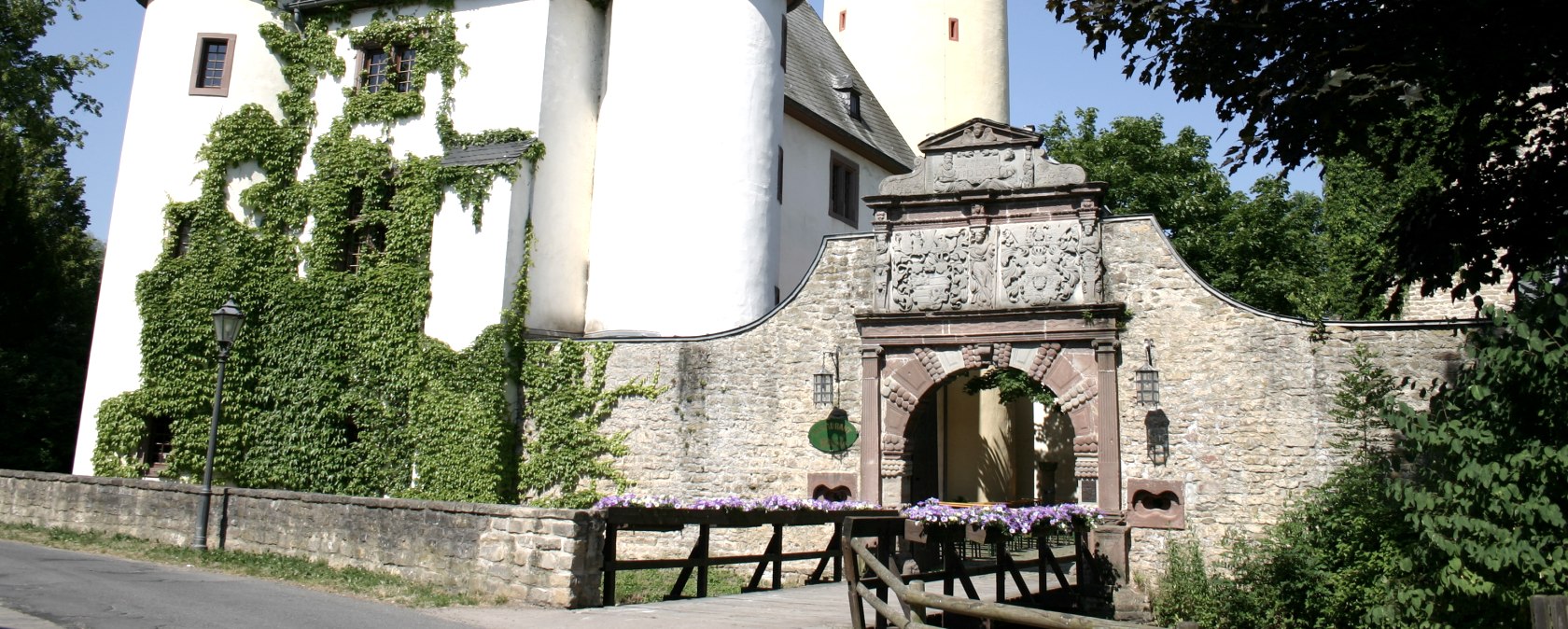 Rittersdorf Castle with two round towers and a high yellow tower. An archway with decorations leads into the castle. Ivy grows on the walls., © Frank Schaal Rittersdorf Castle with two round towers and a high yellow tower. An archway with decorations leads into the castle. Ivy grows on the walls., © Frank Schaal