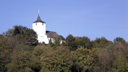 The church of St. Apollonia in Gransdorf is enthroned on a wooded hill under a clear blue sky., © Doris Pauels The church of St. Apollonia in Gransdorf is enthroned on a wooded hill under a clear blue sky., © Doris Pauels