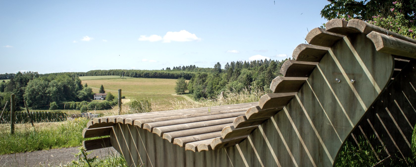 Wooden bench with a view of green fields and forests under a blue sky in Neidenbach., © TI Bitburger Land - Monika Mayer Wooden bench with a view of green fields and forests under a blue sky in Neidenbach., © TI Bitburger Land - Monika Mayer