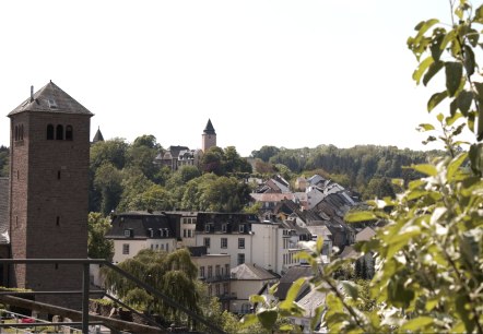 Panoramablick auf Kyllburg mit einem Kirchturm im Vordergrund, umgeben von Häusern und grünen Bäumen unter blauem Himmel., © TI Bitburger Land Panoramablick auf Kyllburg mit einem Kirchturm im Vordergrund, umgeben von Häusern und grünen Bäumen unter blauem Himmel., © TI Bitburger Land