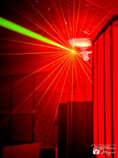 Ein lebhaftes Lichtspiel mit roten und grünen Lasern in einem dunklen Raum. Die Atmosphäre ist festlich und energetisch.