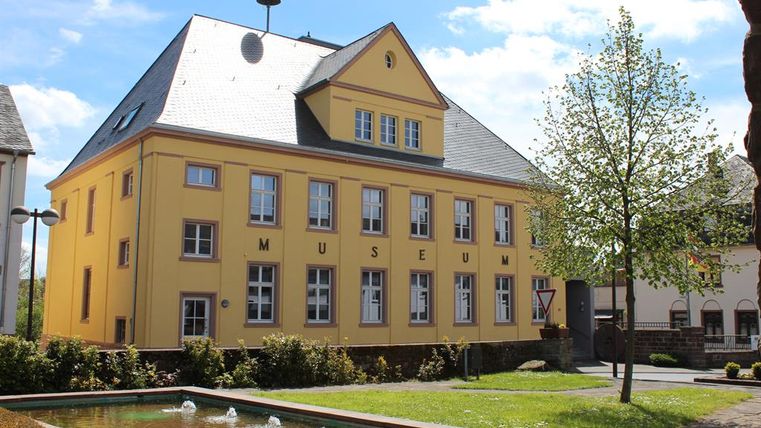 Gelbes Gebäude des Heimatmuseums Speicher mit Brunnen im Vordergrund.