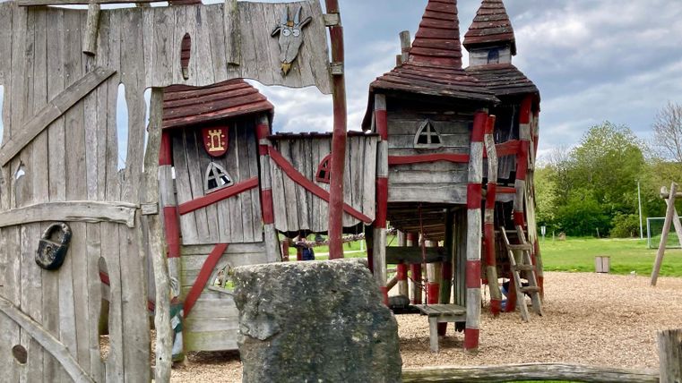 Ein Spielplatz mit einer bunten Holzstruktur in Form von Türmen. Die Holzskulpturen sind rustikal und laden zum Spielen ein.