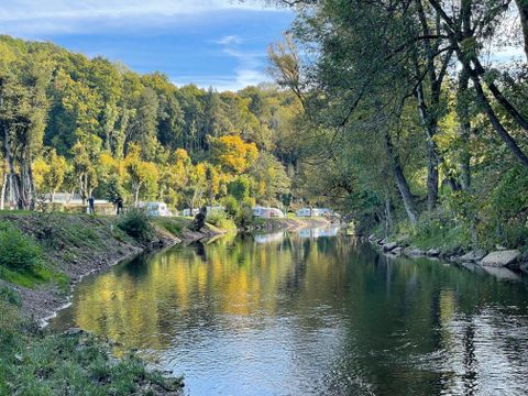 Ein ruhiger Fluss umgeben von bunten Bäumen im Herbst. Im Hintergrund sind einige Wohnwagen entlang des Ufers zu sehen.