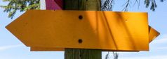 Gelbes Wegweiser-Schild an einem Holzpfosten im Freien.