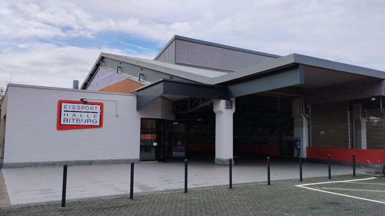 A modern sports center with a large entrance and a clear sky. The facade is in neutral colors and has an inviting character.