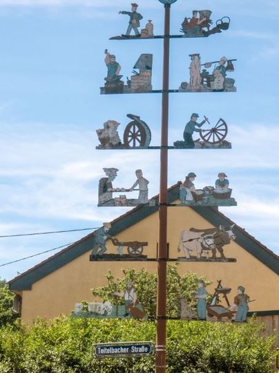 Ein traditioneller Maibaum mit handwerklichen Figuren vor einem Haus in Trimport.