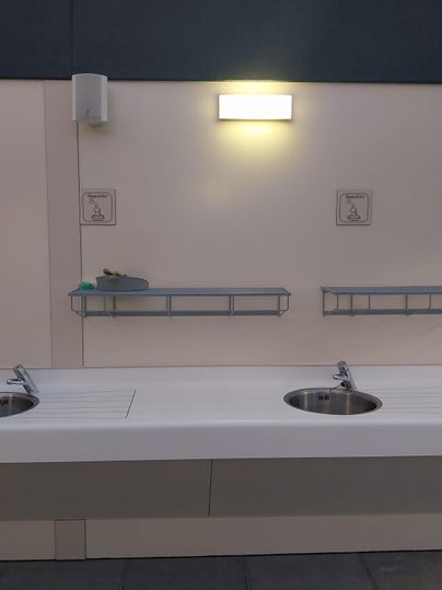 Un lavabo moderne avec deux cuves sur un mur blanc. En haut, il y a deux étagères pour le rangement.