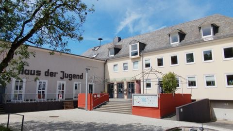 Ein modernes Jugendhaus mit einer freundlichen Fassade und einem einladenden Eingangsbereich. Der Himmel ist klar und die Umgebung ist grün.