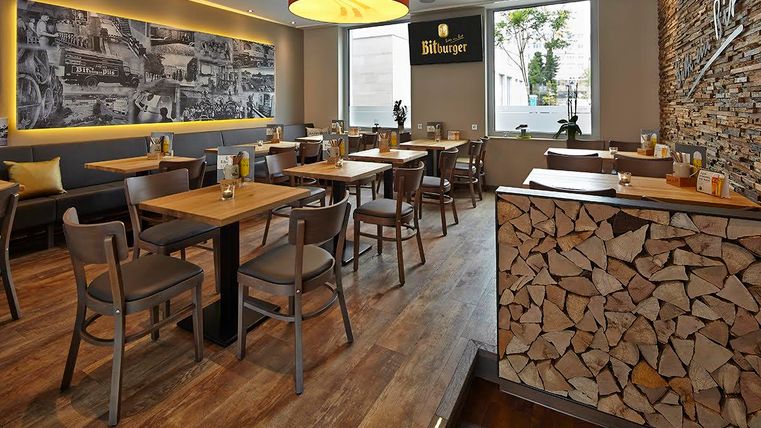 A modern restaurant with wooden floors and cozy tables. A large photograph and a decorative woodpile can be seen on the wall.