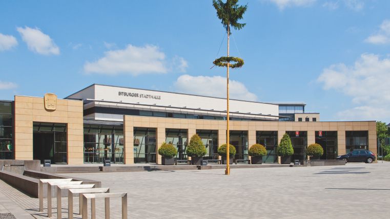 Blick auf die Stadthalle Bitburg mit aufgestelltem Maibaum auf dem Vorplatz