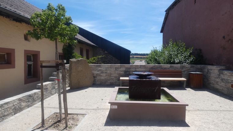 Ein Rastplatz in Trimport mit einem Brunnen, einer Bank und einem Baum.