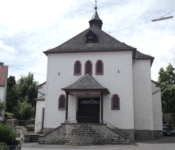 White church in Fließem with a red roof and bell tower, surrounded by trees and neighboring houses. The sky is slightly cloudy., © TI Bitburger Land