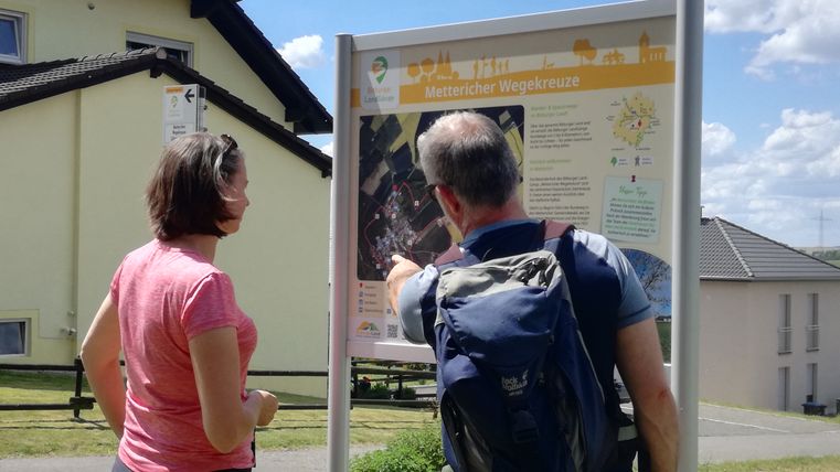 Zwei Personen betrachten eine Wandertafel im Freien.