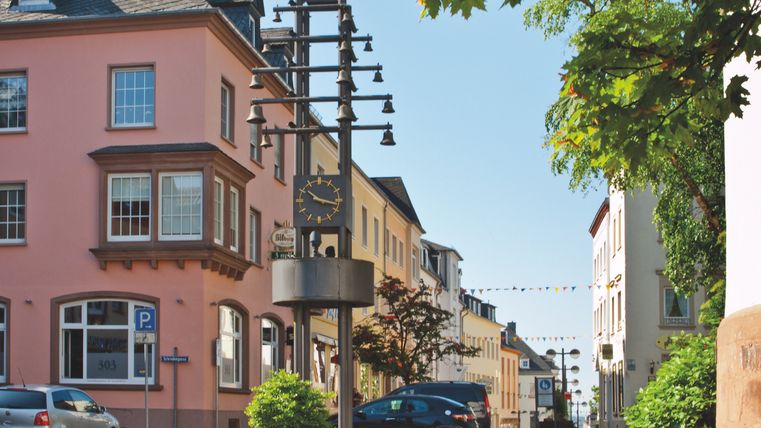 Eine malerische Straße mit bunten Häusern und einer großen Uhr in der Mitte. Die Atmosphäre ist freundlich und einladend.