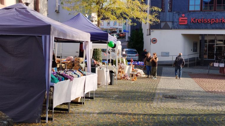 Een wekelijkse markt met meerdere kraampjes en kleurrijke tenten. Mensen slenteren ontspannen langs de straat.