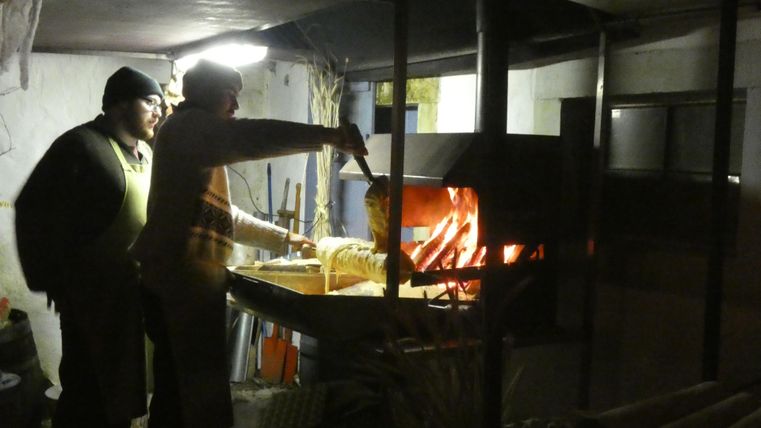 Zwei Männer stehen an einem Grill und bereiten Essen zu. Der Grill ist hell erleuchtet und erzeugt eine warme Atmosphäre.