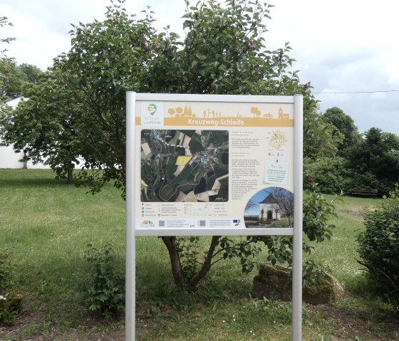 Informationstafel zur Kreuzweg-Schleife in Sefferweich, umgeben von grüner Landschaft und Bäumen., © TI Bitburger Land