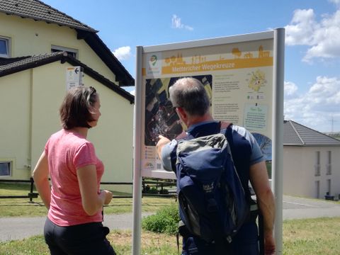 Zwei Personen betrachten eine Wandertafel im Freien.