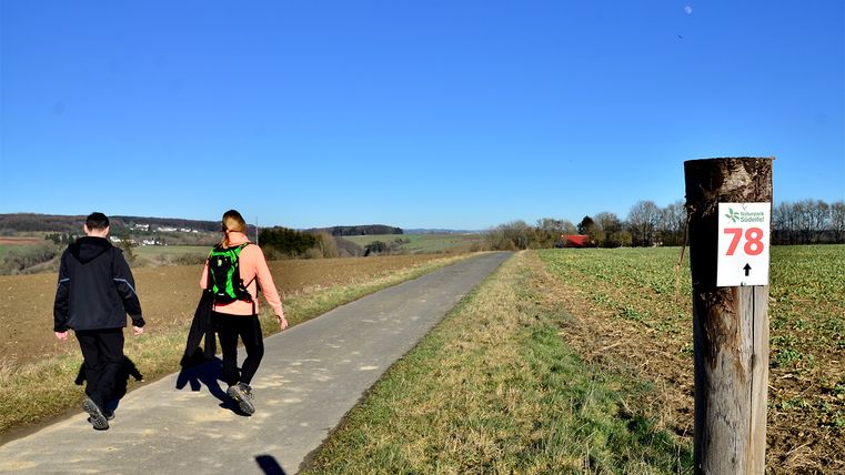 Zwei Personen wandern auf einem Weg im Naturpark Südeifel, neben einem Pfosten mit der Nummer 78.
