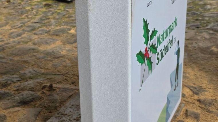 An information sign about nature in a park-like area. The sign has a clear white surface with green and colorful symbols.