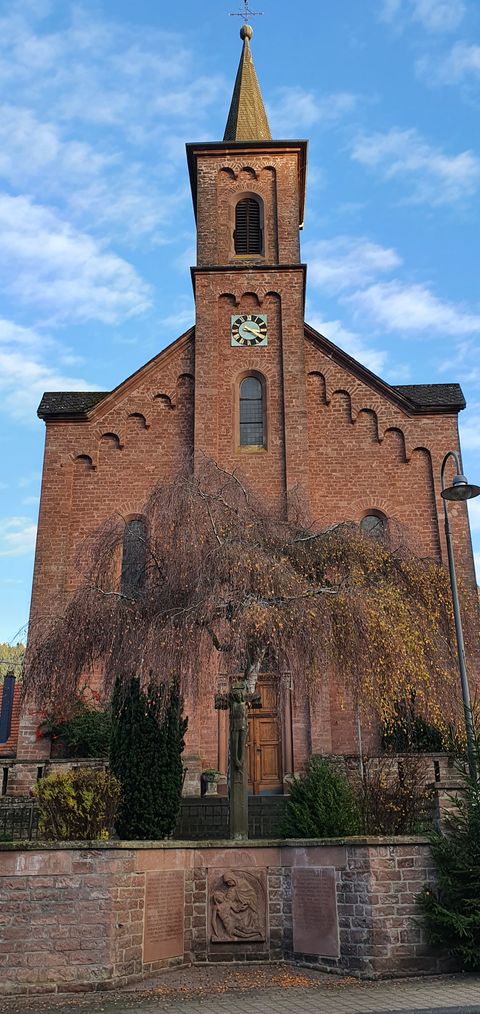 Kirche St. Laurentius mit Turm und Uhr, umgeben von Bäumen.