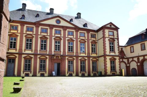 Ein historisches Gebäude mit bunten Fassaden und großen Fenstern. Der Innenhof ist gepflastert und gut beleuchtet von der Sonne.