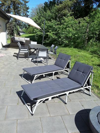 Une terrasse conviviale avec deux chaises longues et un coin repas. Des arbres verts et un temps ensoleillé créent une atmosphère détendue.