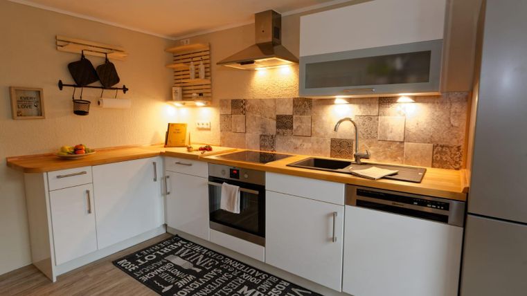 Eine moderne Küche mit einer Holzarbeitsplatte und weißen Schränken. Sie verfügt über einen Herd, ein Waschbecken und eine ansprechende Fliesenauswahl.