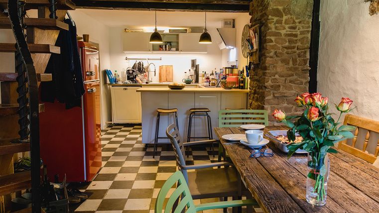 Eine gemütliche Küche mit Holzstuhl und Tisch, dekoriert mit frischen Blumen. Im Hintergrund ist eine moderne Kücheneinrichtung sichtbar.