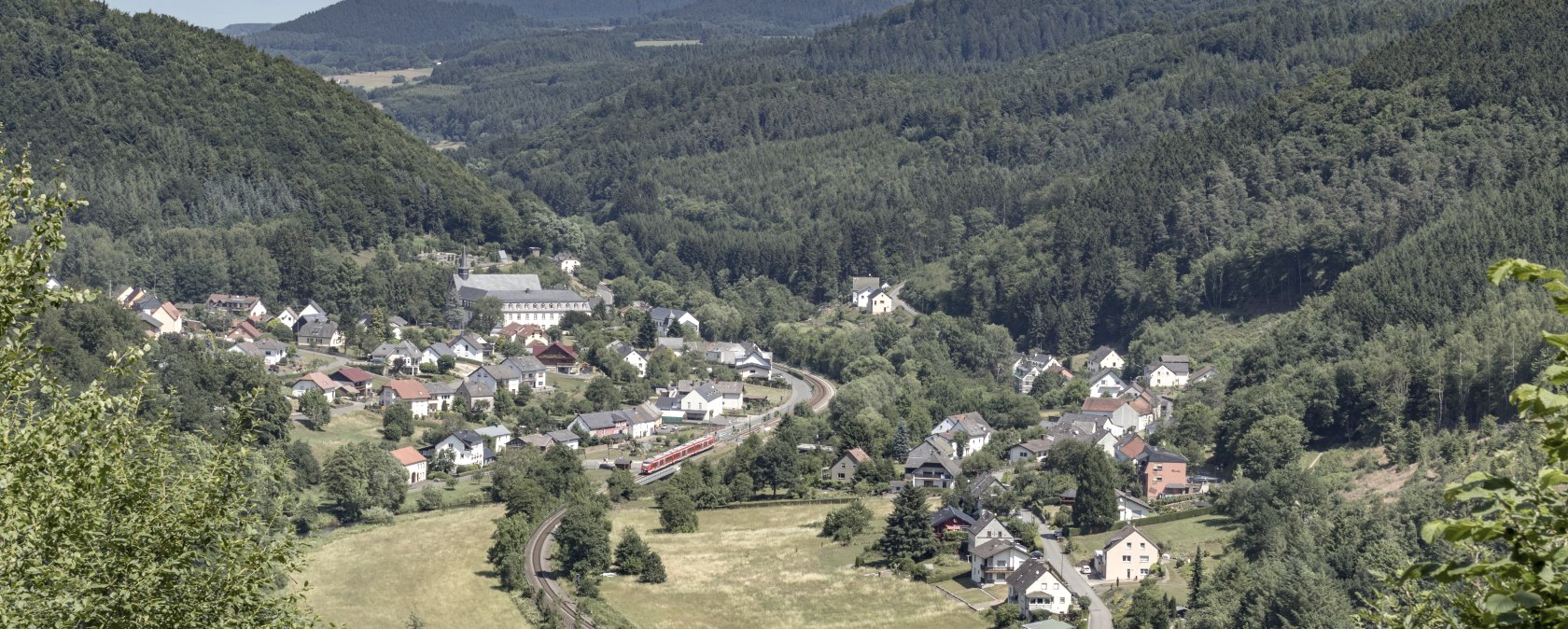 Panoramic view of a village in a green valley, surrounded by wooded hills and meadows. A train runs through the village., © Rudolf Höser