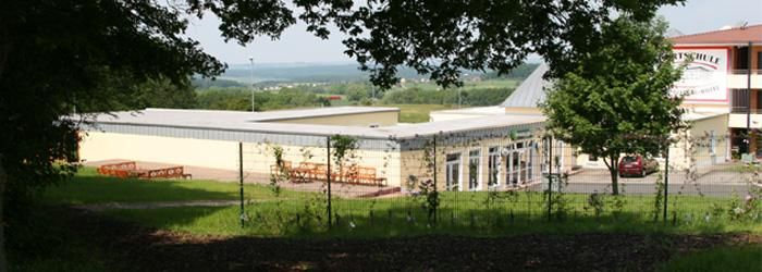 Ein modernes Gebäude, umgeben von Bäumen und einem weiten Ausblick auf die Landschaft. Die Terrasse lädt zum Verweilen ein.