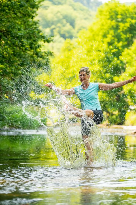 Eine Frau wirbelt in dem Fluss Prüm Wasser mit ihren Füßen auf