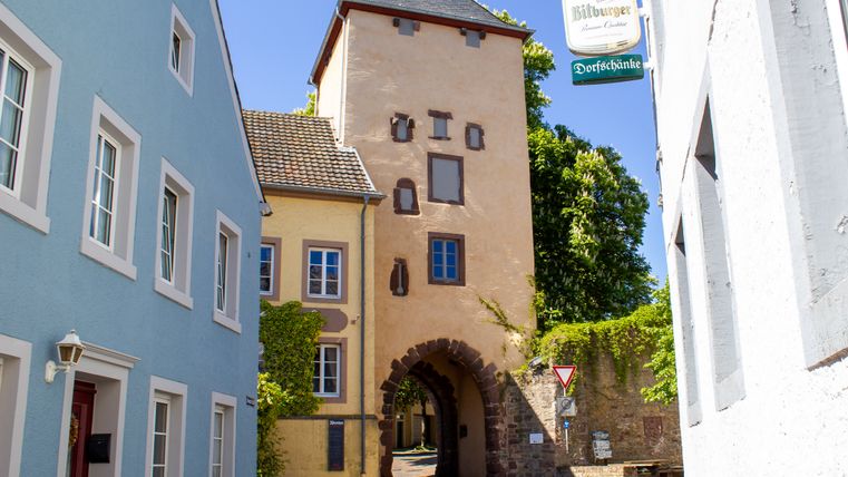 Historisches Stadttor in Dudeldorf mit angrenzenden bunten Häusern und einem Schild der Dorfschänke.