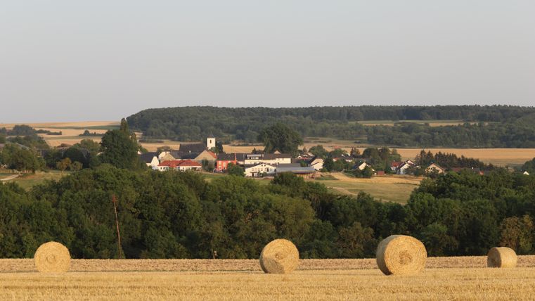 Landschaft mit Strohballen und Dorf im Hintergrund.