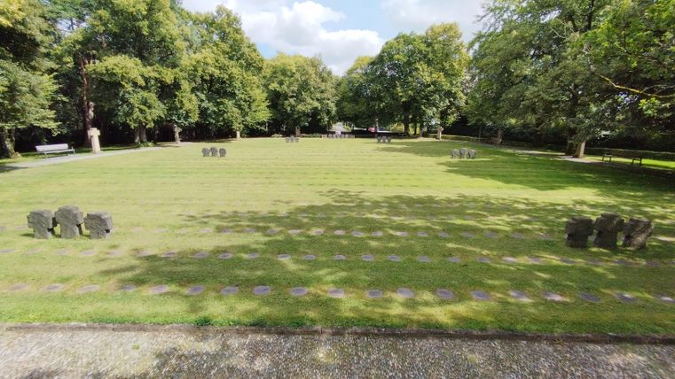 Ein ruhiger Park mit viel Grün und Schatten von Bäumen. Auf dem Rasen sind einige Steinskulpturen zu sehen.