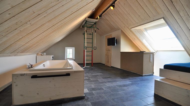 A stylish attic room with wooden walls and a modern bathroom. There is a bathtub and plenty of daylight through the windows.