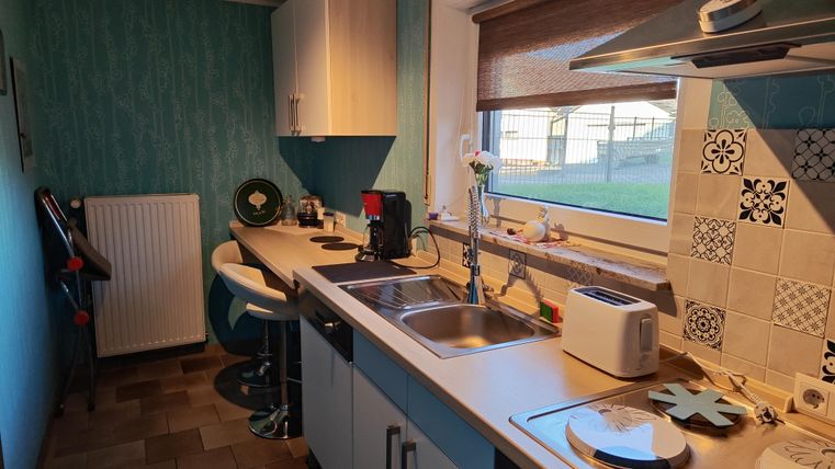 Eine moderne Küche mit blauen Wänden und einer hellen Arbeitsplatte. Sie ist ausgestattet mit einem Herd, einer Spüle und modernen Küchengeräten.