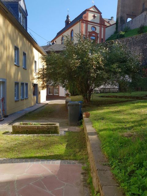 Een rustige binnenplaats met een groen gazon, een vuilcontainer en een bloemenperkje. Op de achtergrond is een historisch gebouw zichtbaar.