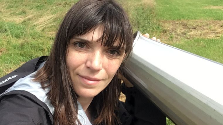 Frau hält ein großes Hörrohr an ihr Ohr in einer grünen Wiesenlandschaft.