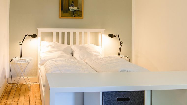 Ein gemütliches Schlafzimmer mit einem Doppelbett und modernen Nachttischen. Die Wände sind hell und es gibt ein Kunstwerk über dem Bett.