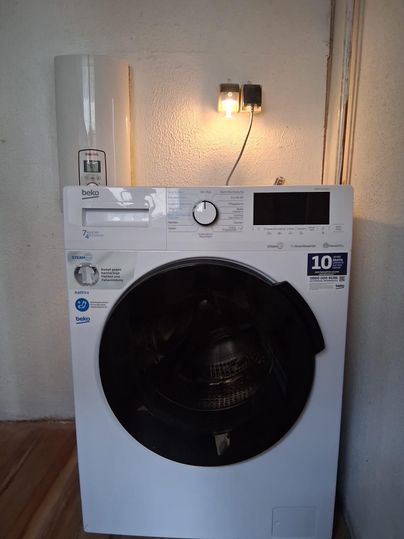 Eine moderne Waschmaschine in Weiß steht an einer Wand. Sie hat ein großes Bullauge und ein digitales Bedienfeld.