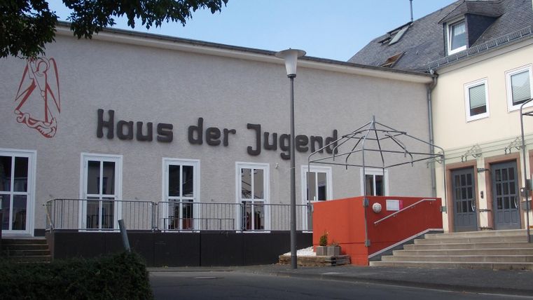 A modern building with a striking facade and the inscription "House of Youth". In front of the entrance, there is a red staircase and some trees in the surrounding area.