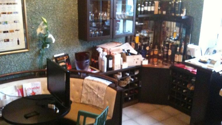 Ein gemütlicher Raum mit einem kleinen Tisch und Stühlen. An der Wand stehen Regale mit Weinflaschen und anderen Getränken.