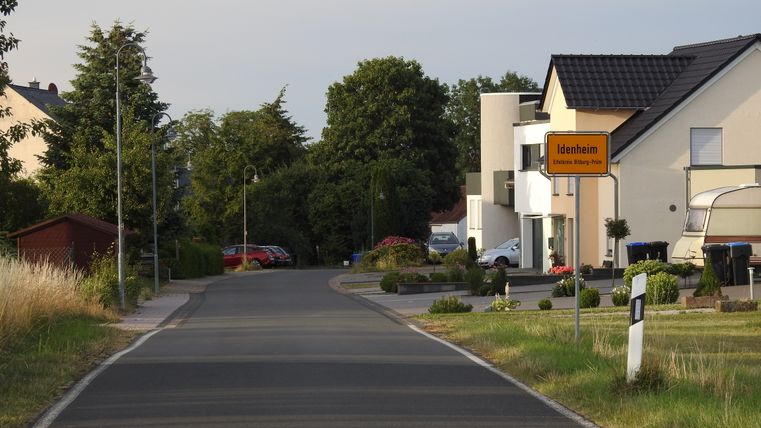 Ortseingang von Idenheim mit Straßenschild und Wohnhäusern.